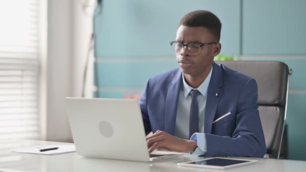 Молодий африканський бізнесмен, який страждає від болю Нека, користуючись ноутбуком у офісі — стокове відео