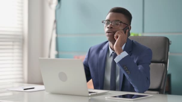 Νεαρός Αφρικανός Επιχειρηματίας Μιλώντας στο τηλέφωνο, ενώ χρησιμοποιεί το Laptop στο Γραφείο — Αρχείο Βίντεο