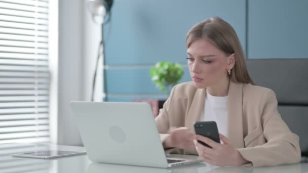 İş kadını ofiste dizüstü bilgisayar kullanırken Smartphone kullanıyor — Stok video