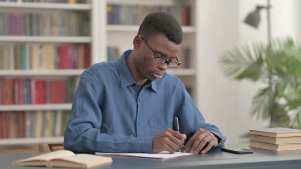 Młody Afrykanin pisanie na papierze w biurze — Wideo stockowe