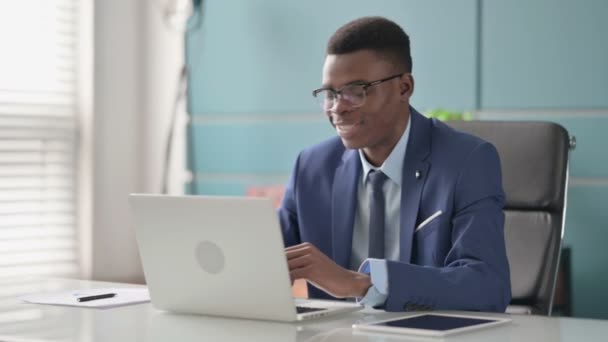 Joven empresario africano hablando en videollamada en el ordenador portátil en la oficina — Vídeos de Stock