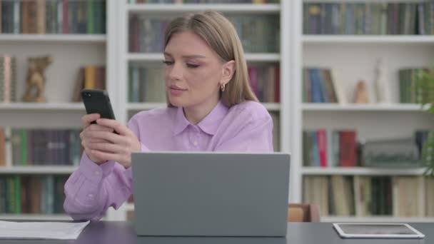 Frau benutzt Smartphone während sie Laptop im Büro benutzt — Stockvideo