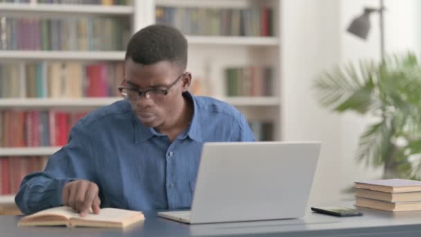 Young African Man Lezen Boek en Werken op Laptop in Office — Stockvideo
