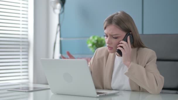 Donna d'affari arrabbiata che parla su smartphone durante l'utilizzo del computer portatile in ufficio — Video Stock