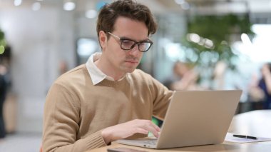 Ofiste dizüstü bilgisayarda çalışan genç adam. 