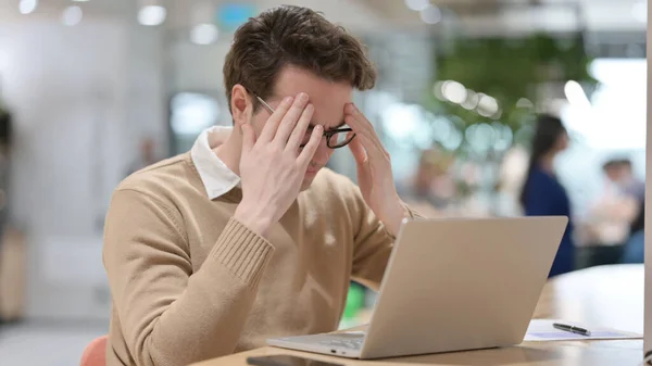 Homem jovem com dor de cabeça enquanto trabalhava no laptop — Fotografia de Stock