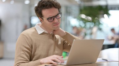 Dizüstü bilgisayarda çalışırken boynu ağrıyan genç adam. 