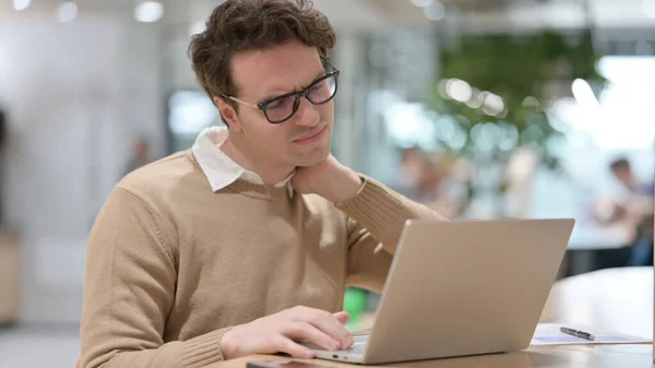 Hombre joven que tiene dolor de cuello mientras trabaja en el ordenador portátil — Foto de Stock