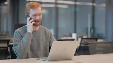 Ofiste dizüstü bilgisayar kullanırken konuşan genç adam.