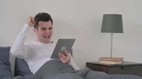 Ο άνθρωπος γιορτάζει την επιτυχία στο Tablet, ενώ κάθεται στο κρεβάτι — Φωτογραφία Αρχείου