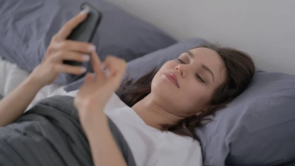 Femme utilisant un téléphone intelligent pendant qu'elle dort au lit — Photo