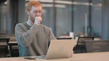 Ofiste dizüstü bilgisayar kullanırken öksüren genç adam. 