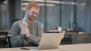 Ofiste dizüstü bilgisayar kullanırken bilek ağrısı çeken genç adam. 