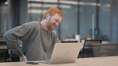 Ofiste dizüstü bilgisayar kullanırken sırt ağrısı çeken genç adam.