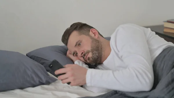 Homem usando Smartphone enquanto dorme na cama — Fotografia de Stock