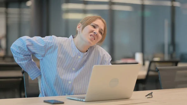 Mulher nova que tem dor nas costas ao usar o portátil no escritório — Fotografia de Stock