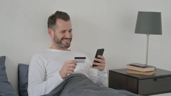 Man Shopping Online with Smartphone in Bed — ストック写真