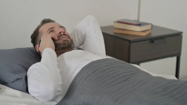 Ο άνθρωπος που μιλάει για κλήση στο Smartphone στο κρεβάτι — Φωτογραφία Αρχείου