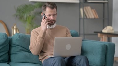Dizüstü bilgisayarlı bir adam telefonda konuşuyor. 