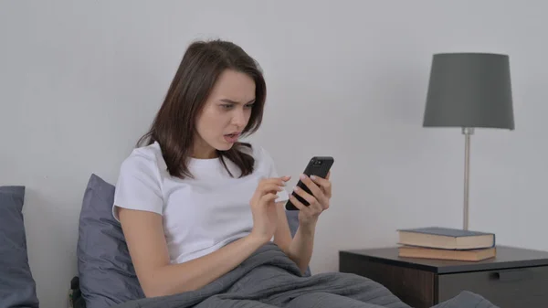 Vrouw reageert op verlies op Smartphone in bed — Stockfoto