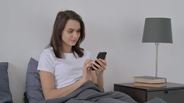 Mulher usando smartphone na cama — Fotografia de Stock