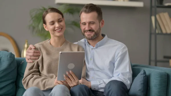 Casal fazendo chamada de vídeo no Tablet enquanto sentado no sofá — Fotografia de Stock