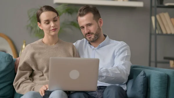 Casal trabalhando no laptop juntos enquanto sentado no sofá — Fotografia de Stock