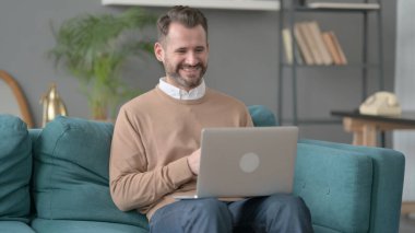 Kanepede bilgisayar başında video çağrısı yapan adam. 