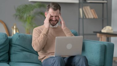 Dizüstü bilgisayarı olan adamın koltukta başı ağrıyor. 