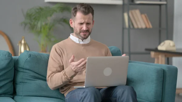 Uomo con computer portatile che reagisce alla perdita sul divano — Foto Stock