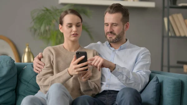 Retrato de casal usando Smartphone enquanto sentado no sofá — Fotografia de Stock