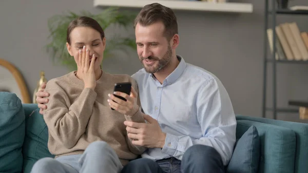 Retrato do casal comemorando o sucesso no smartphone, sentado no sofá — Fotografia de Stock