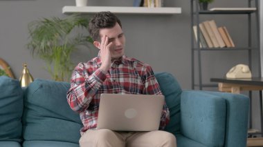 Dizüstü bilgisayarı olan adamın koltukta başı ağrıyor. 