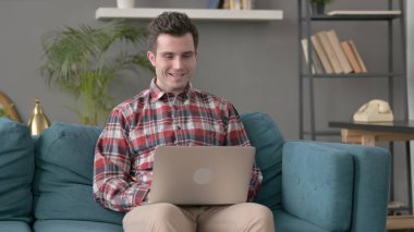 Kanepede bilgisayar başında video çağrısı yapan adam. 