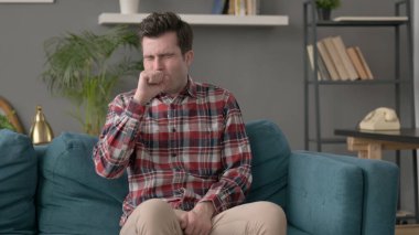 Kanepede oturan adam öksürüyor. 