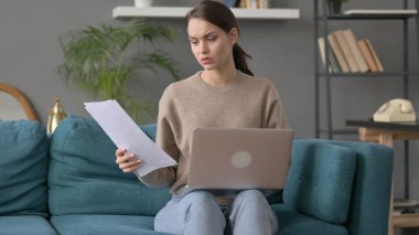 Dizüstü bilgisayarlı bir kadın Kanepede Belgeler üzerinde çalışıyor 