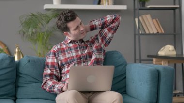 Dizüstü bilgisayarı olan adamın koltukta boynu ağrıyor. 