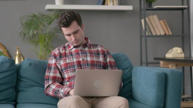 Dizüstü bilgisayarı olan adam koltukta kestiriyor. 