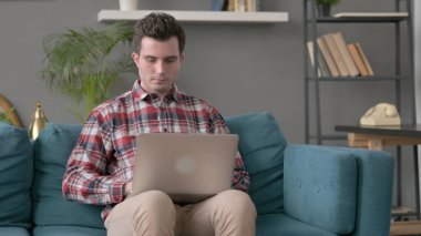 Kanepede oturan adam, dizüstü bilgisayar açılıyor.