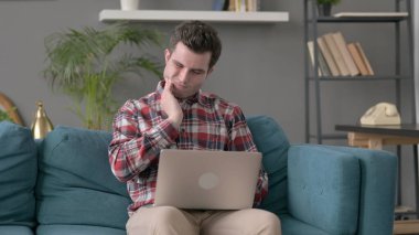 Dizüstü bilgisayarı olan adamın koltukta dişi ağrıyor. 