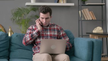 Dizüstü bilgisayarlı kızgın adam telefonda konuşuyor. 