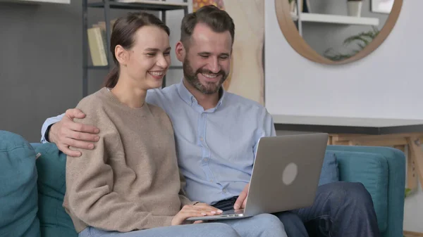 Casal fazendo chamadas de vídeo on-line no laptop, sentado no sofá — Fotografia de Stock