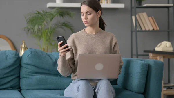 Femme avec ordinateur portable en utilisant Smartphone sur canapé — Photo