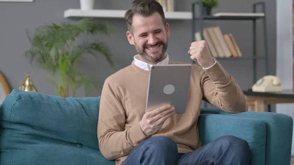 Uomo che celebra il successo sul tablet sul divano — Foto Stock