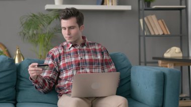 Kanepeye dizüstü bilgisayarda ödeme yapan adam. 