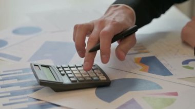 Close up of Middle Aged Businessman Writing on Paper, using Calculator