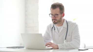 Doctor Smiling at Camera while using Laptop in Office