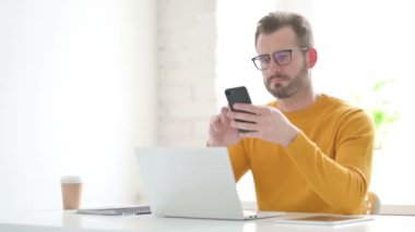 Ofiste dizüstü bilgisayar kullanırken akıllı telefon kullanan adam 