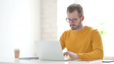 Ofiste dizüstü bilgisayar kullanırken kameraya gülümseyen adam