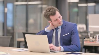 Ofiste dizüstü bilgisayar kullanırken boyun ağrısı çeken bir iş adamı. 